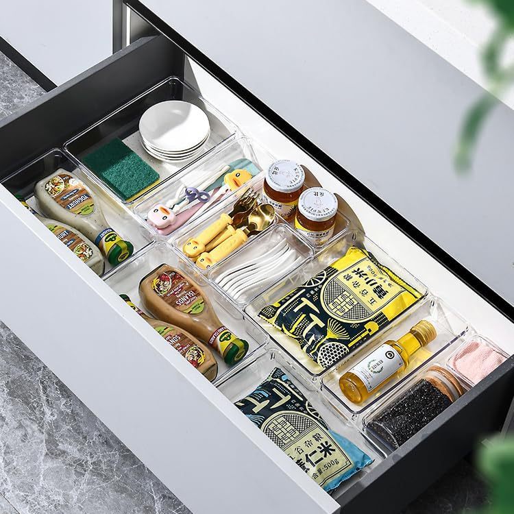 Clear drawer organizer trays holding kitchen gadgets, sauces and spices in a drawer