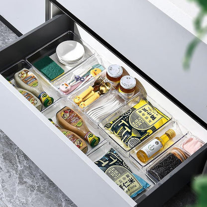 Clear drawer organizer trays holding kitchen gadgets, sauces and spices in a drawer
