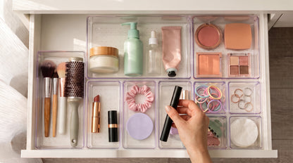 Hand taking a mascara from clear organizer trays in a vanity drawer