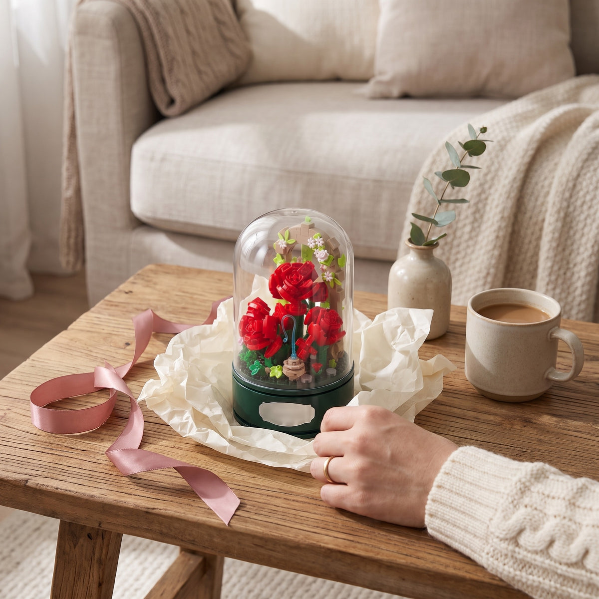 The rose music box as a gift on tissue paper, a hand resting beside it