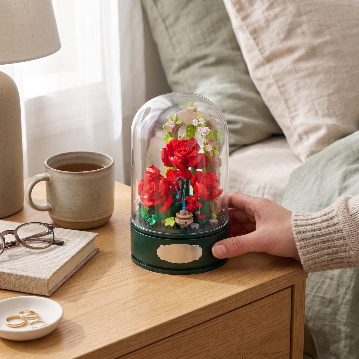 A hand lifting the clear dome off the Rose Garden Music Box on a shelf