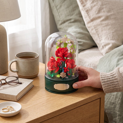 A hand lifting the clear dome off the Rose Garden Music Box on a shelf