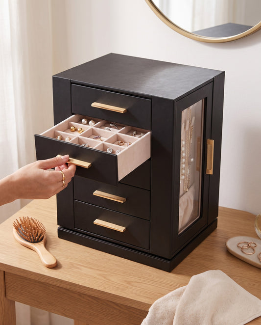 A hand sliding out a drawer of the jewelry cabinet, the clear side door showing necklaces