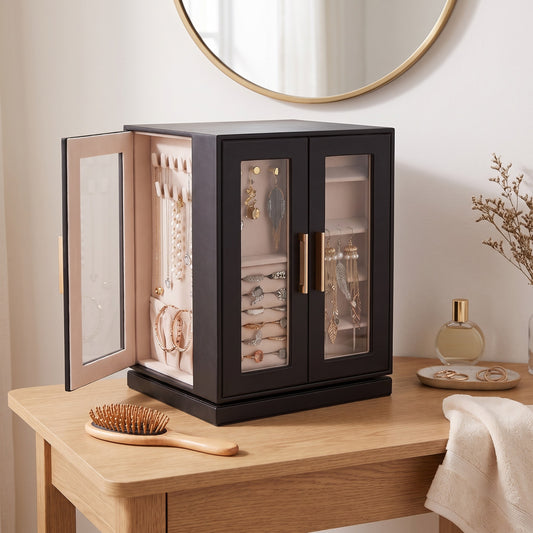 Black rotating jewelry cabinet on an oak dressing table, side door open on necklaces, rings and earrings behind clear doors