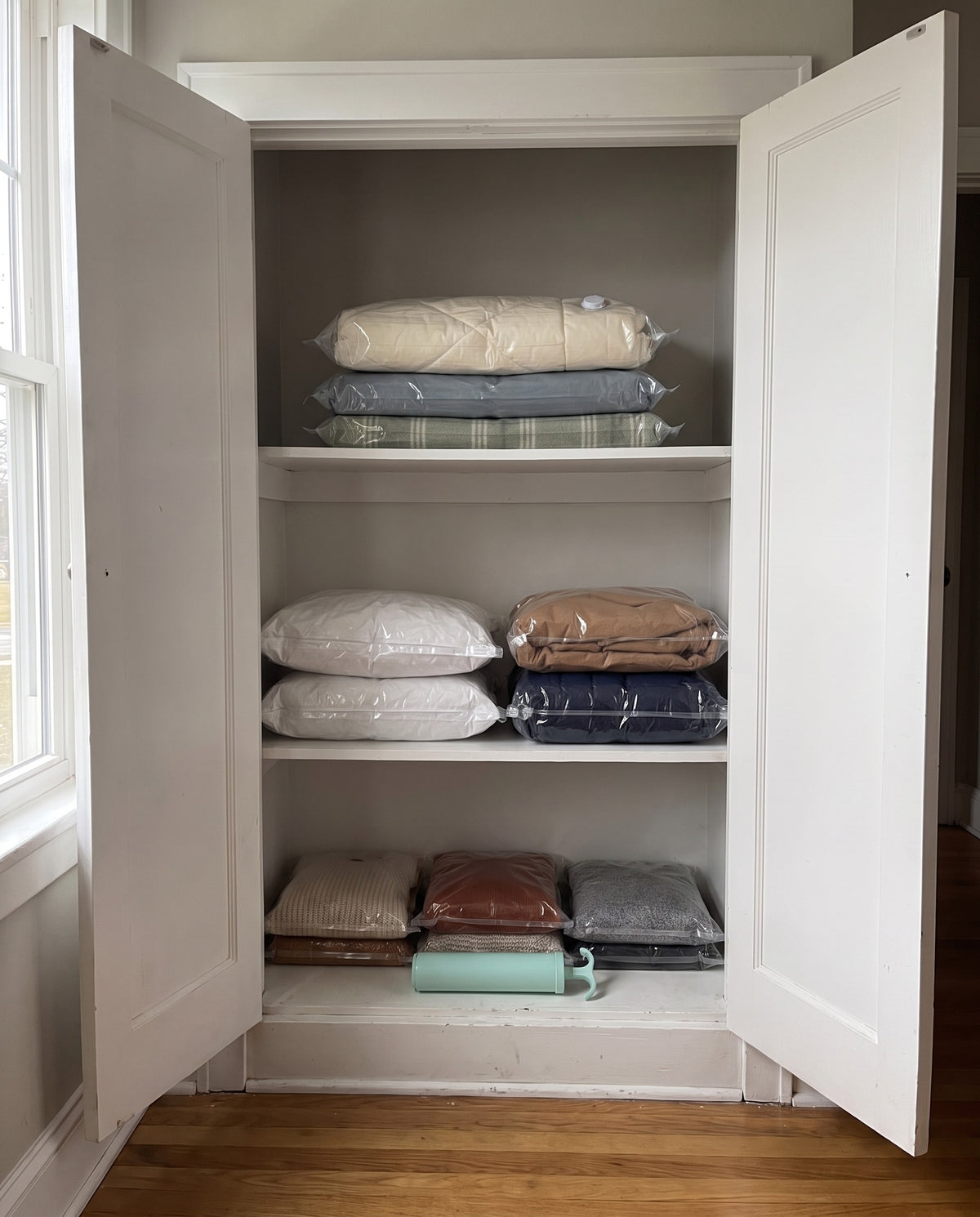 After: the same closet with comforters, pillows, coats and sweaters sealed flat in clear vacuum bags and the hand pump on the bottom shelf
