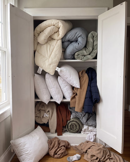Before: a linen closet overflowing with puffy comforters, pillows, coats and sweaters spilling onto the floor